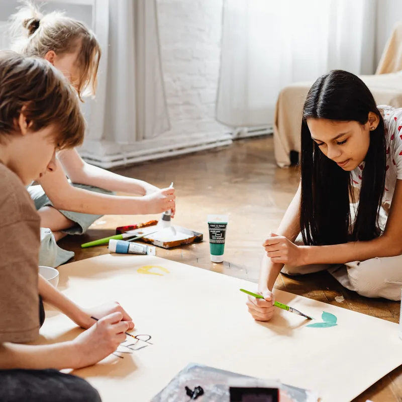 Three children painting a poster together on the floor